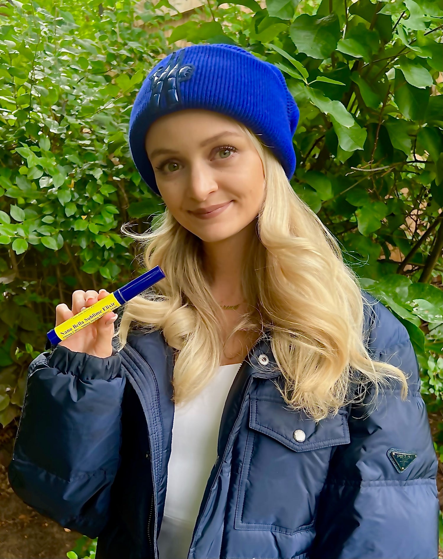 woman in blue hat holding nano bella nano cbg sublime elixir in front of trees